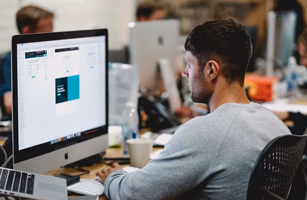 Man sitting on a desk working on an iMac
