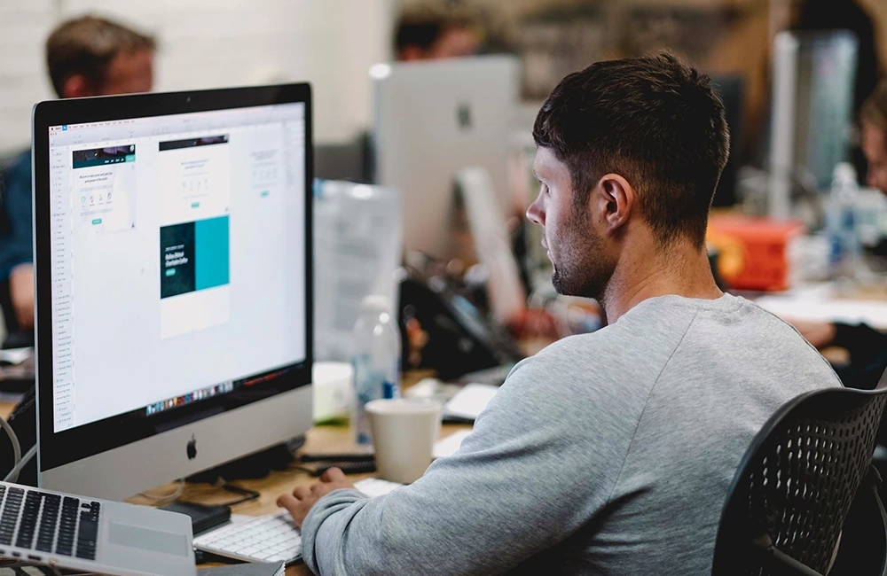 Man sitting on a desk working on an iMac
