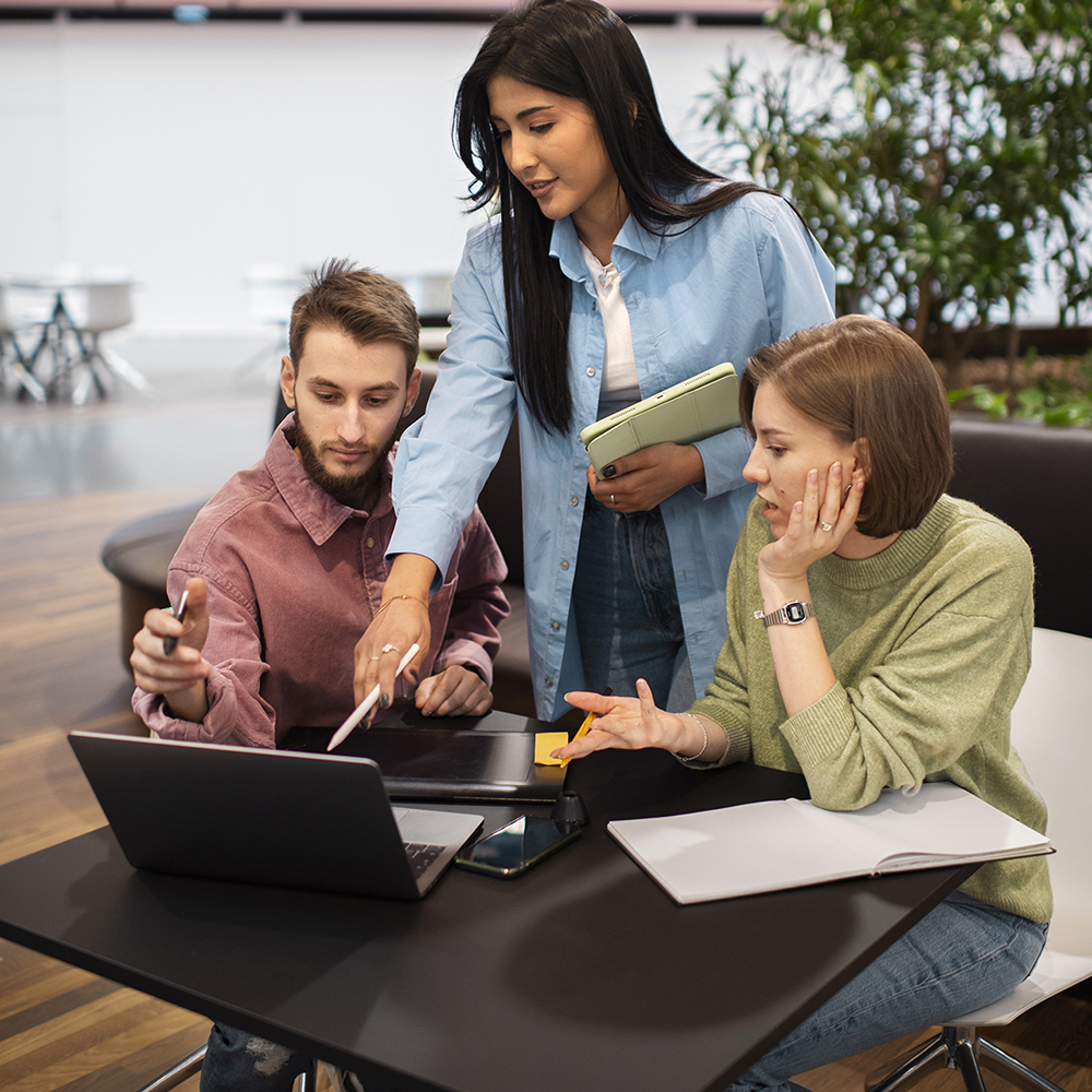 Woman holding an iPad pointing at something on a Mac computer